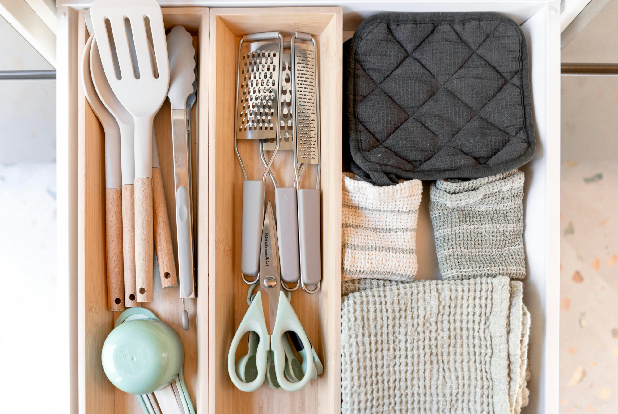 Kitchen drawer with wooden organizer trays holding utensils and folded towels